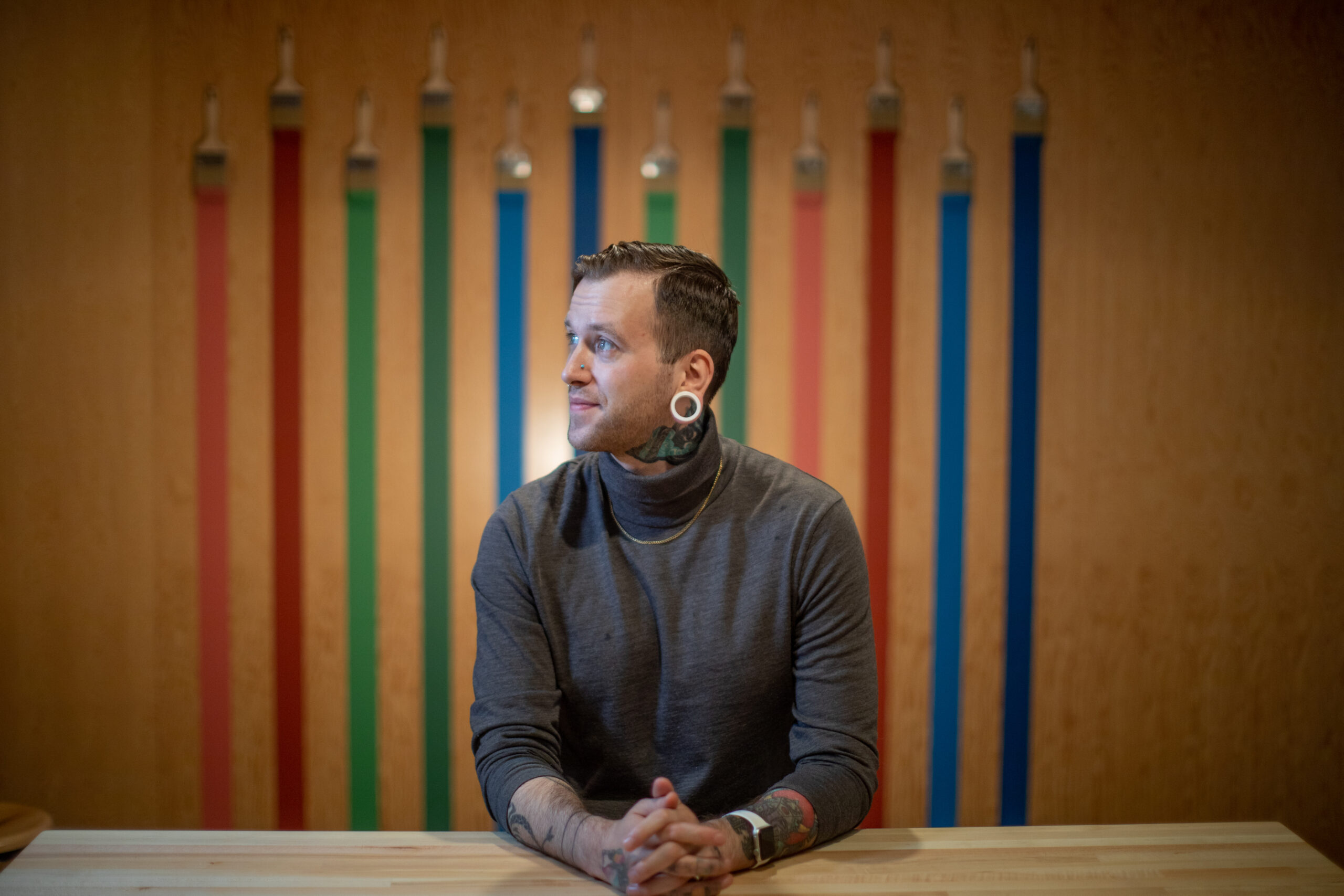 A professional photo taken of Liam Flowers, who sits at a table in a gray turtleneck.